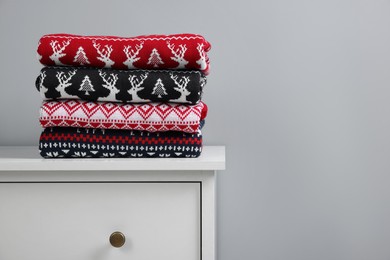 Photo of Different folded Christmas sweaters on chest of drawers against grey background. Space for text