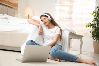 Photo of Lazy young woman with laptop and headphones in bedroom