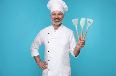 Photo of Happy chef in uniform with kitchen utensils on light blue background