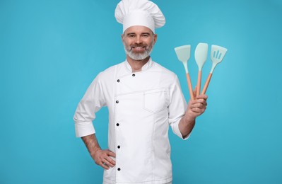 Happy chef in uniform with kitchen utensils on light blue background