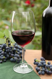 Photo of Red wine and grapes on wooden table outdoors, closeup