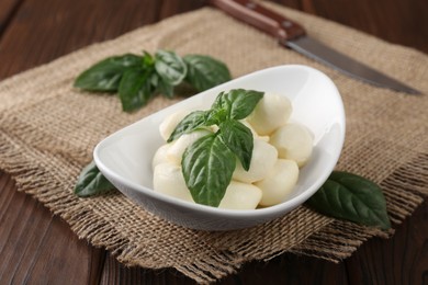 Tasty mozarella balls and basil leaves in bowl on wooden table