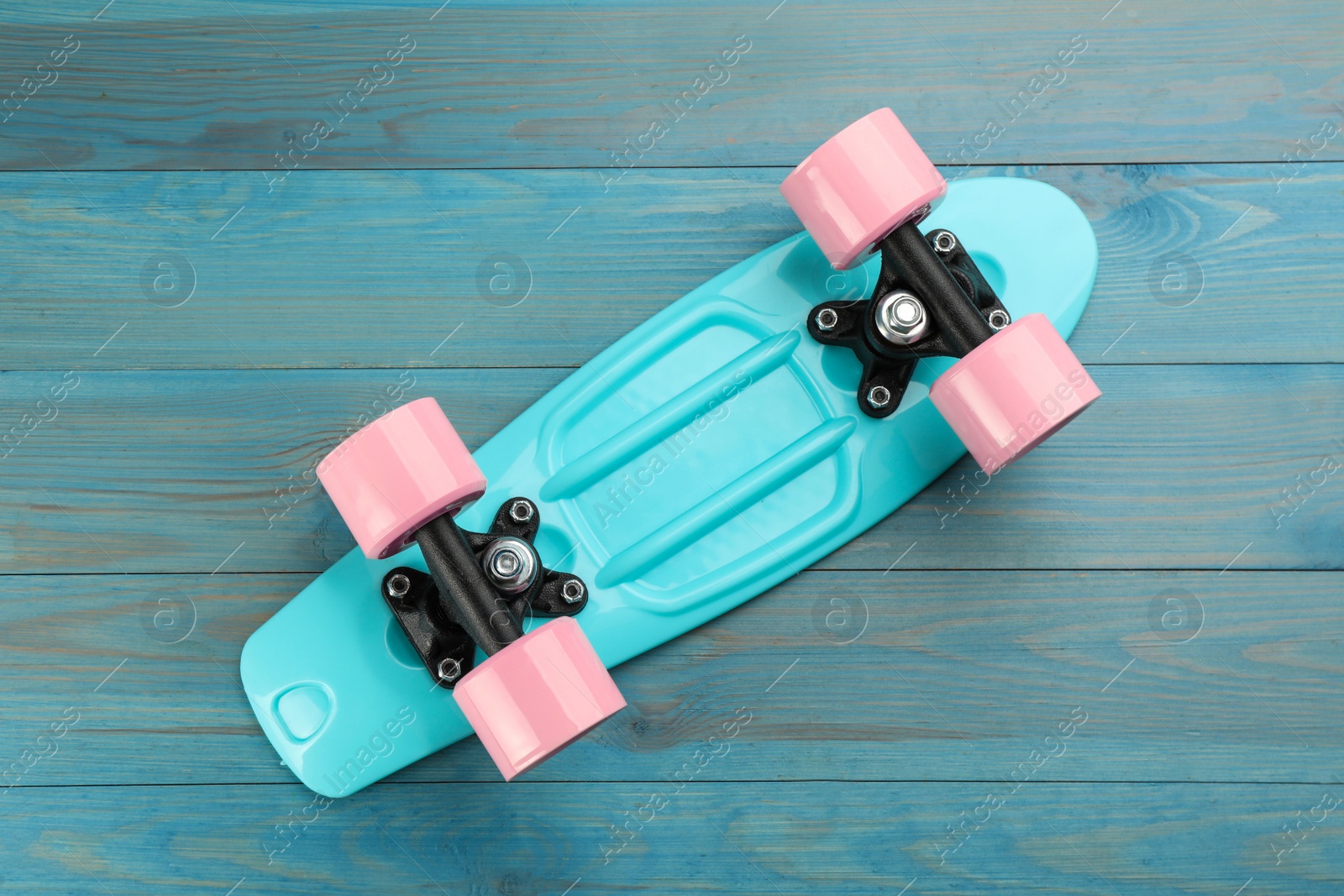 Photo of Bright skateboard on turquoise wooden background, top view. Sport equipment