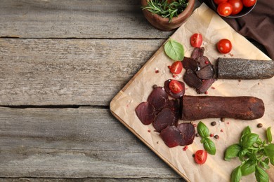 Photo of Delicious dry-cured beef basturma with basil, tomatoes and spices on wooden table, flat lay. Space for text