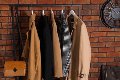 Photo of Coat rack with clothes near brick wall in hallway. Interior design