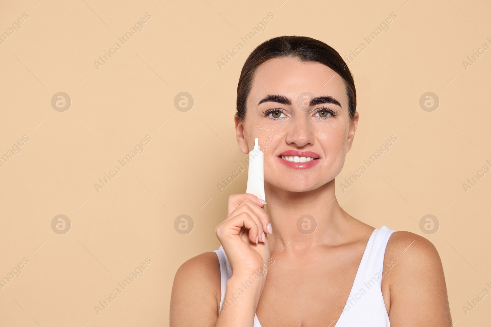 Photo of Woman with cosmetic product around eye on beige background. Space for text