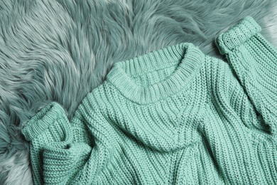 Photo of Soft knitted sweater on green fur rug, flat lay