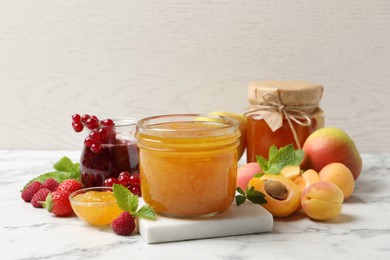 Photo of Jars with different jams and fresh fruits on white marble table