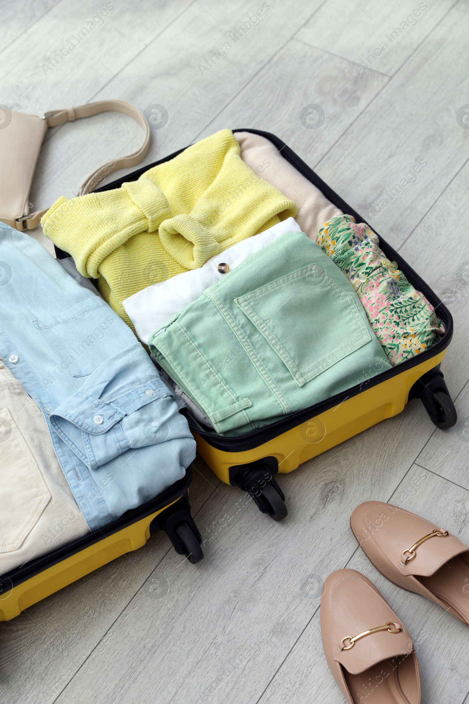 Photo of Open suitcase packed for trip, handbag and shoes on floor