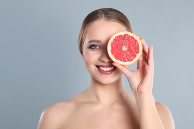 Photo of Young woman with cut grapefruit on grey background. Vitamin rich food