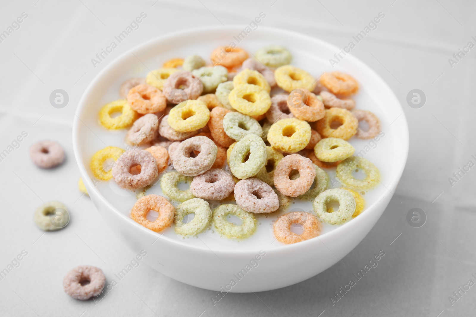 Photo of Cereal rings and milk in bowl on white tiled table, closeup