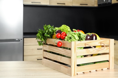 Wooden crate with vegetables on table in kitchen. Space for text