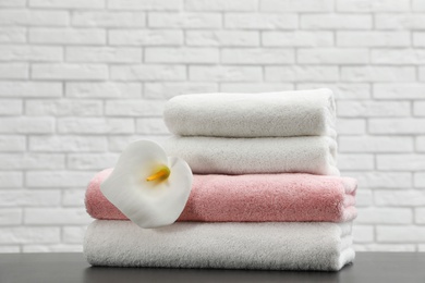 Photo of Stack of folded soft towels with flower on table near brick wall