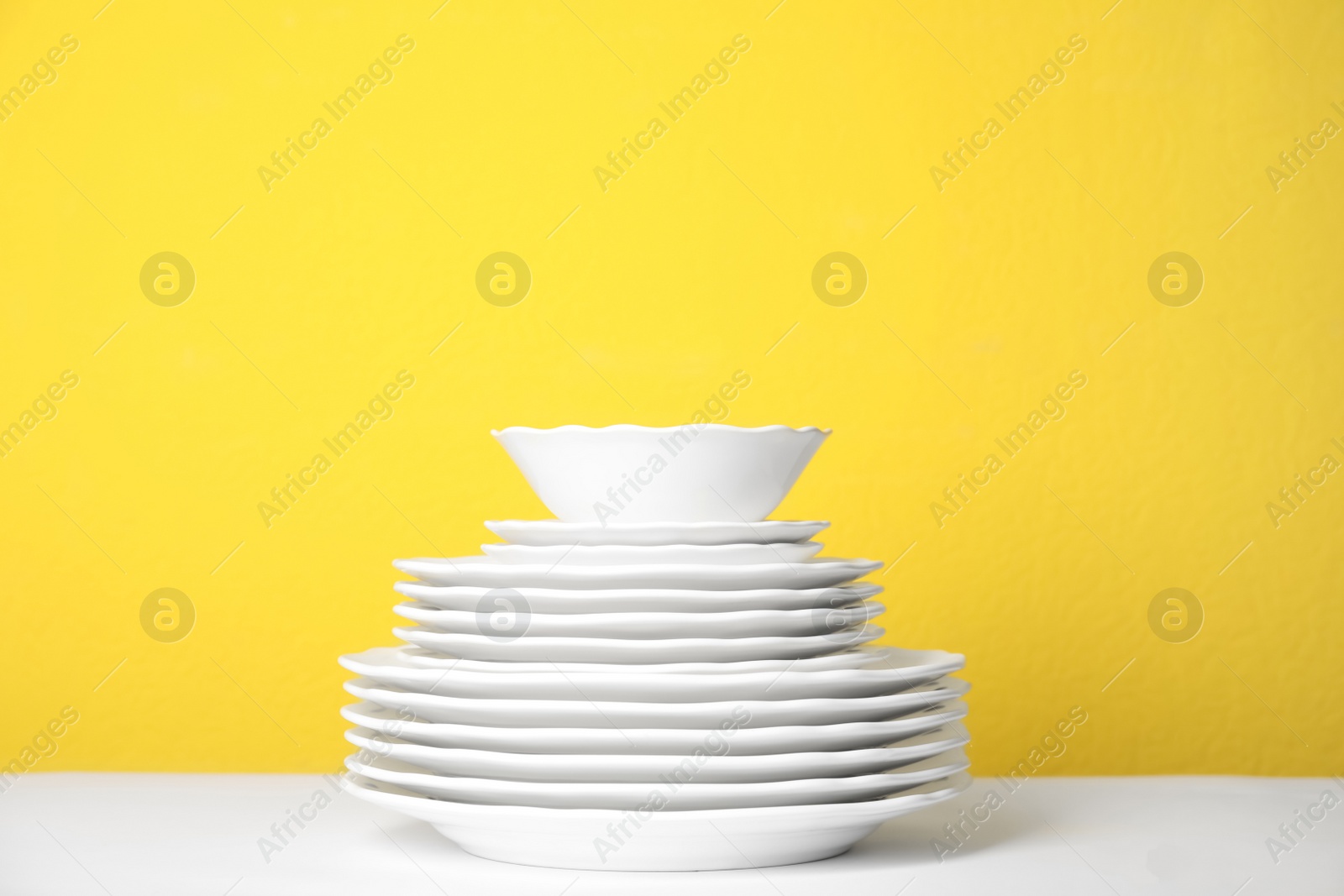 Photo of Stack of clean plates on white table against yellow background