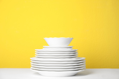 Photo of Stack of clean plates on white table against yellow background