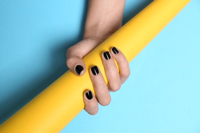 Photo of Woman with black manicure holding paper roll on color background, closeup. Nail polish trends