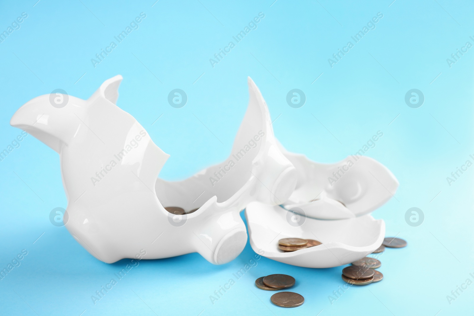 Photo of Broken piggy bank with coins on light blue background