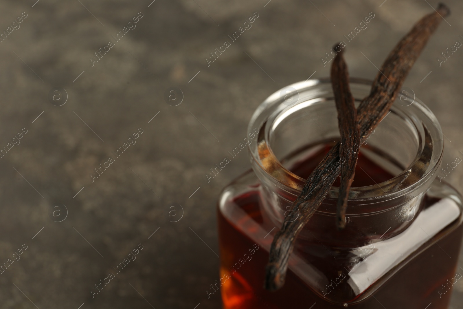 Photo of Aromatic homemade vanilla extract and dry pods on grey table, closeup. Space for text