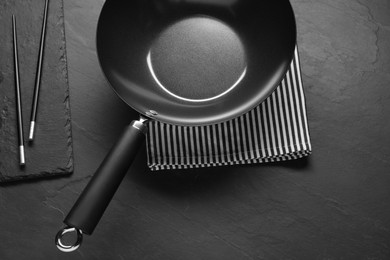 Photo of Empty iron wok and chopsticks on black table, flat lay