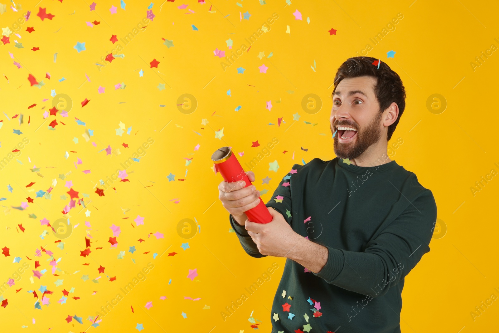 Photo of Emotional man blowing up party popper on yellow background