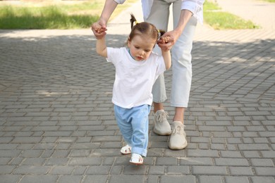 Photo of Mother supporting daughter while she learning to walk outdoors, closeup