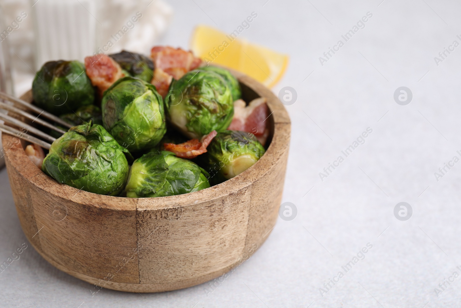 Photo of Delicious roasted Brussels sprouts and bacon in bowl on light table, closeup. Space for text