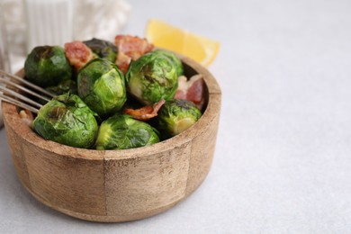 Photo of Delicious roasted Brussels sprouts and bacon in bowl on light table, closeup. Space for text