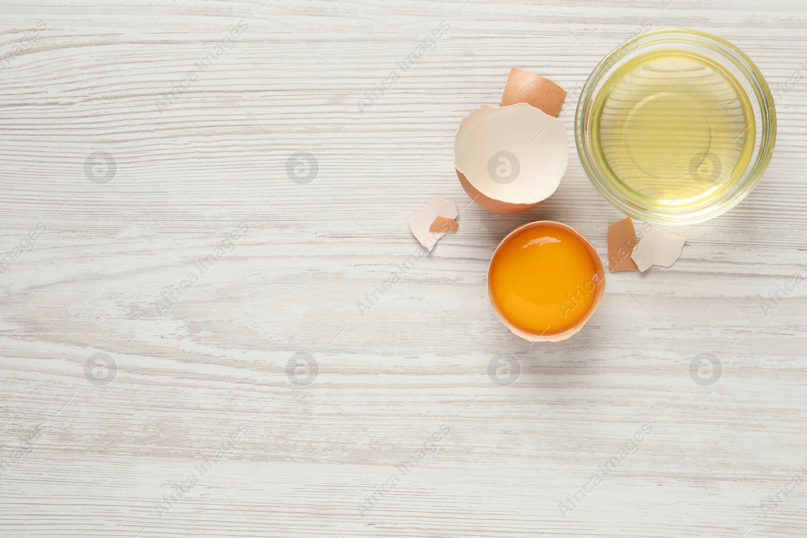 Photo of Yolk in broken chicken eggshell and bowl with white on wooden table, flat lay. Space for text