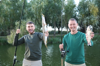 Friends with fishing rods and catch at riverside. Recreational activity