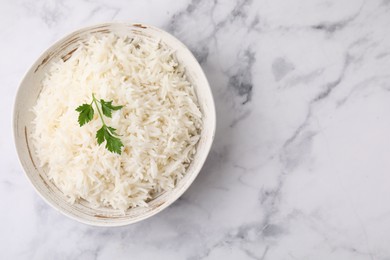 Photo of Bowl of delicious rice with parsley on white marble table, top view. Space for text