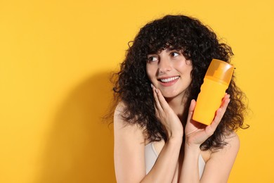 Beautiful young woman holding bottle of sun protection cream on orange background, space for text