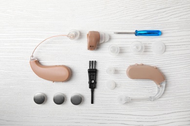 Photo of Flat lay composition with hearing aids and accessories on white wooden background
