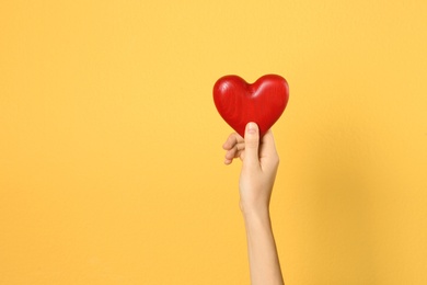 Woman holding decorative heart in hand on color background, space for text