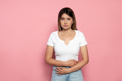 Young woman suffering from menstrual pain on pink background
