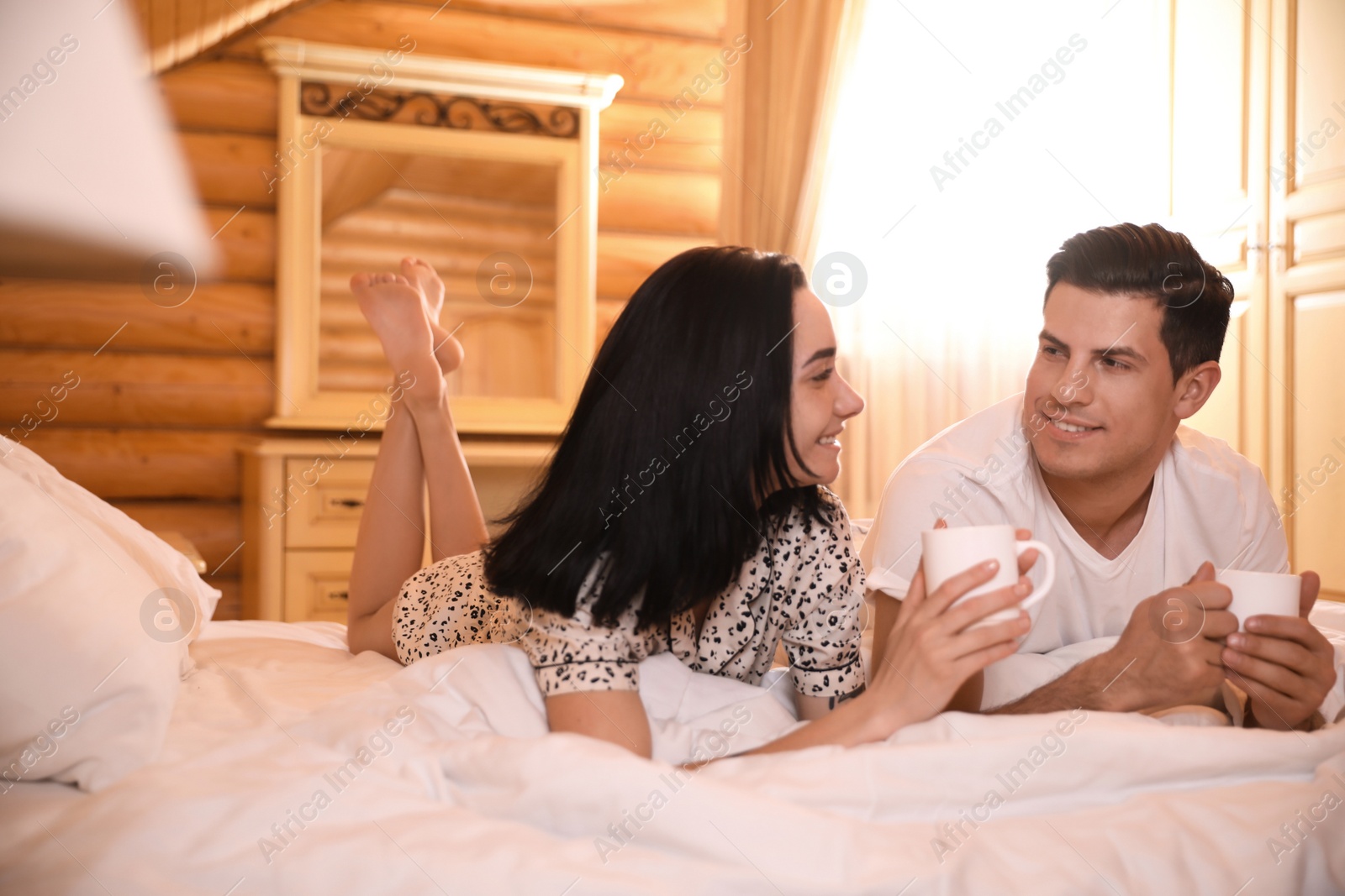 Photo of Couple with drinks lying in bed at home. Lazy morning