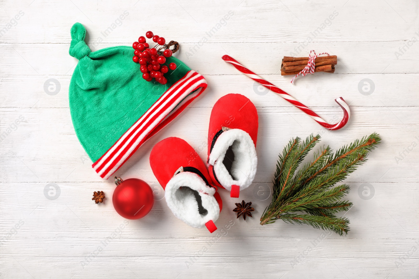 Photo of Cute baby booties, small elf hat and Christmas decorations on white wooden background, flat lay