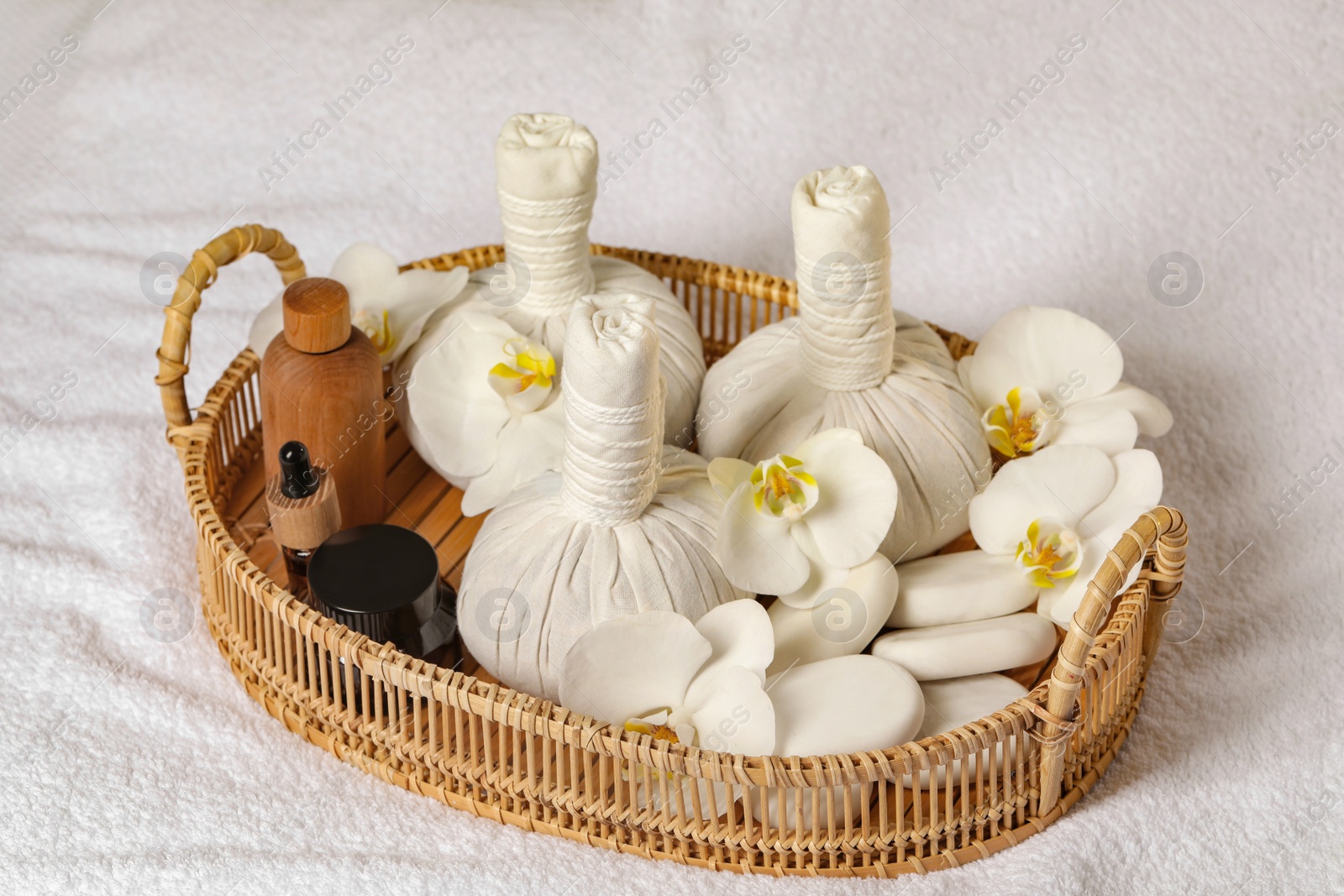 Photo of Wicker tray with herbal bags and other spa products on white bath towel