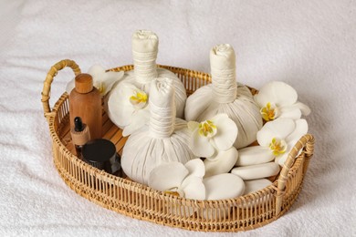 Wicker tray with herbal bags and other spa products on white bath towel