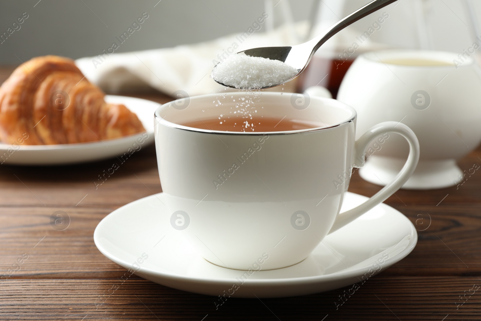 Photo of Adding sugar into cup of tea at wooden table, closeup