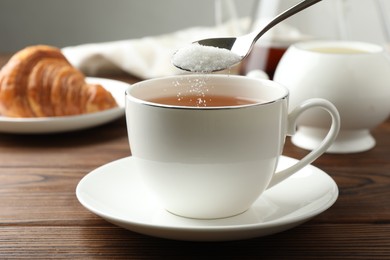 Photo of Adding sugar into cup of tea at wooden table, closeup