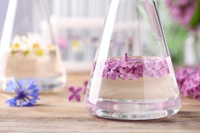 Photo of Flask with lilac flowers on wooden table, closeup. Essential oil extraction