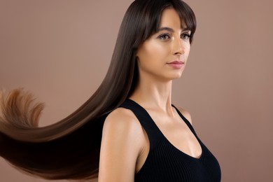 Hair styling. Attractive woman with straight long hair on pale brown background