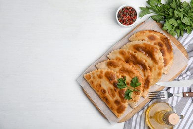 Photo of Delicious fried chebureki and ingredients served on white table, flat lay. Space for text