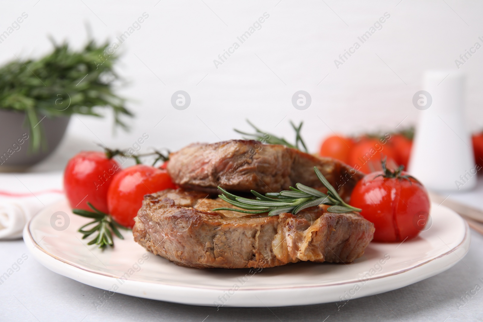 Photo of Delicious fried meat with rosemary and tomatoes on white table, closeup