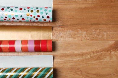 Photo of Different colorful wrapping paper rolls on wooden table, flat lay. Space for text