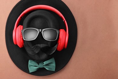 Photo of Man's face made of artificial mustache, sunglasses and hat on brown background, top view. Space for text