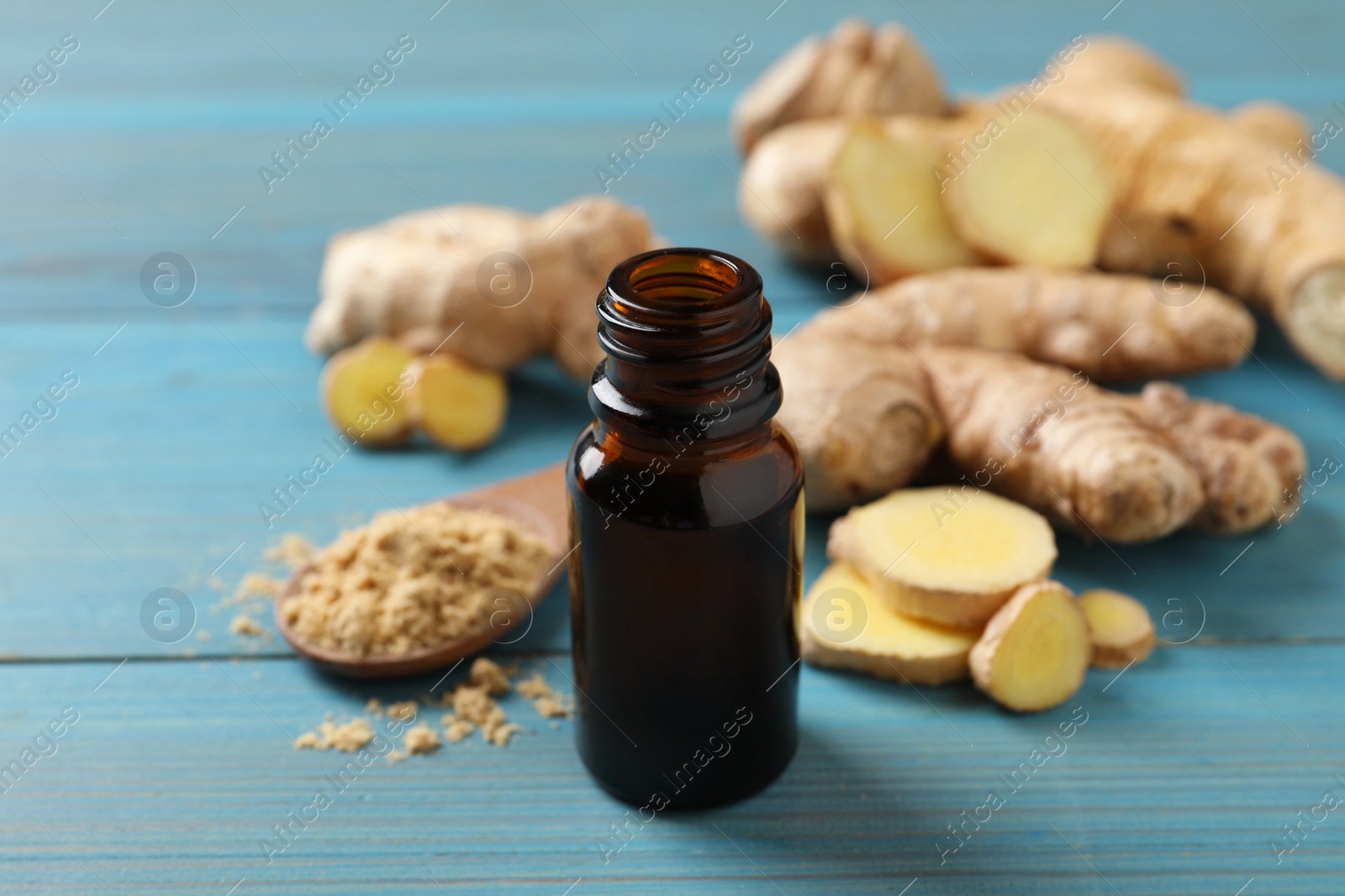 Photo of Glass bottle of essential oil and ginger root on light blue wooden table
