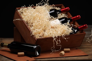 Box with wine bottles on wooden table against black background