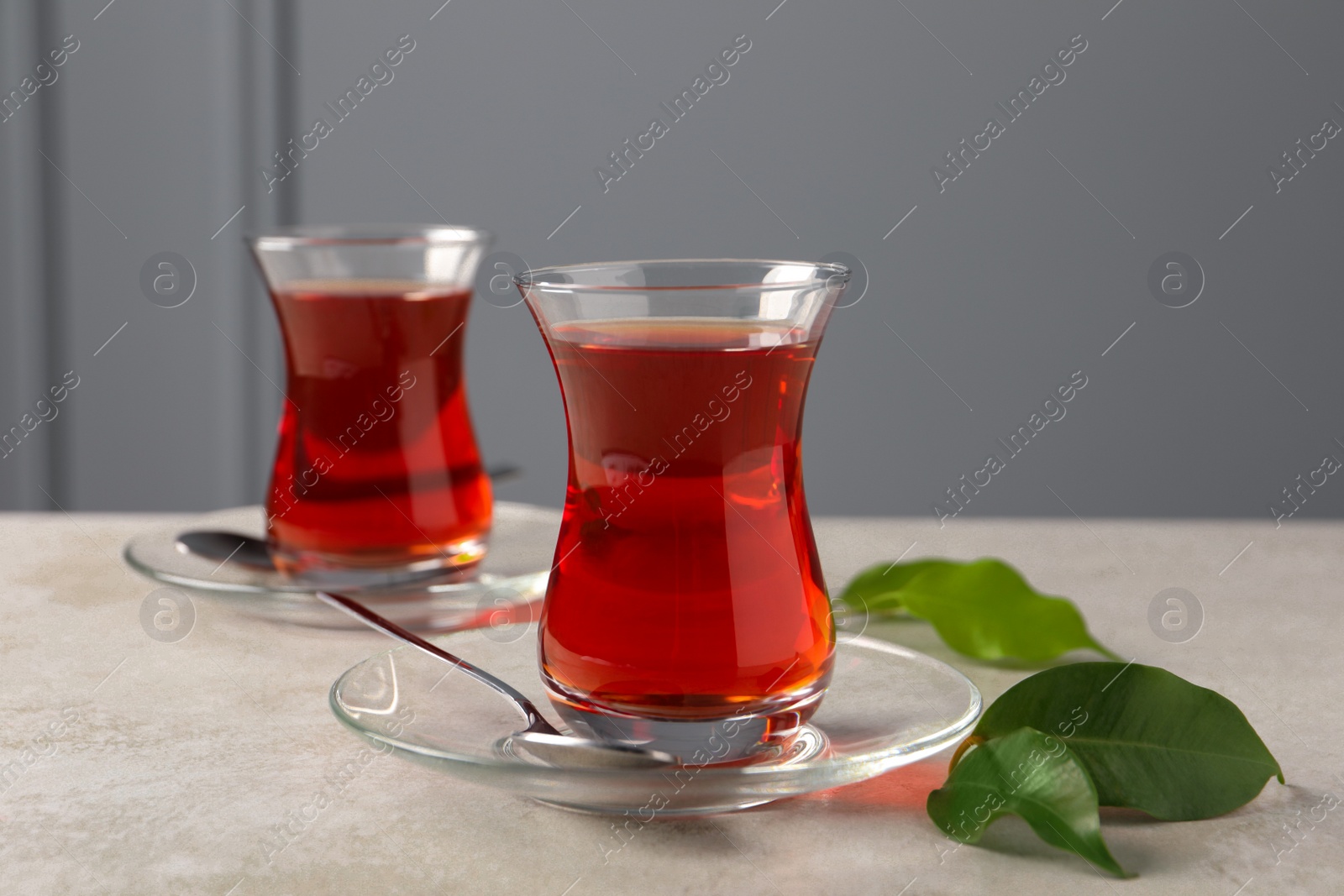 Photo of Glasses with traditional Turkish tea and green leaves on light grey table