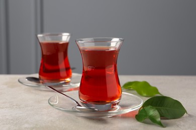 Photo of Glasses with traditional Turkish tea and green leaves on light grey table